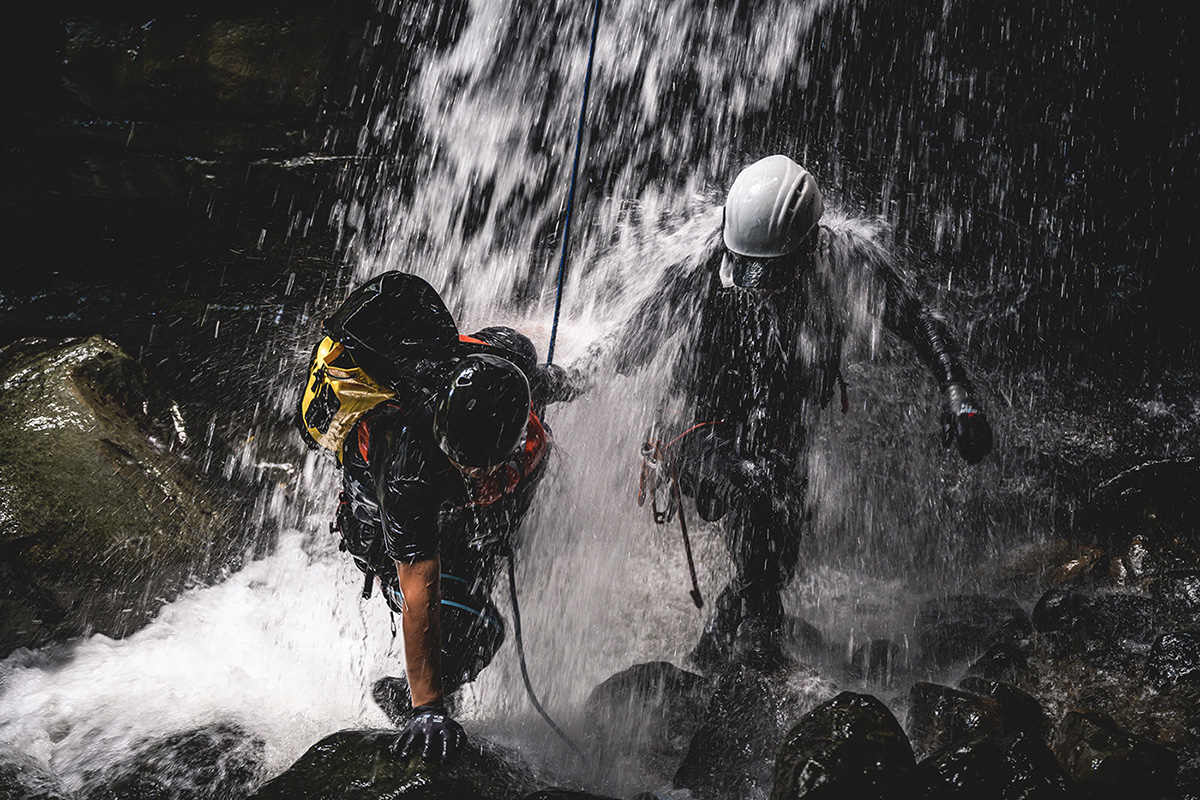 Canyoner on ropes beside a mossy waterfall in a tight Dominican gorge, canyoning in dominica adventure trips through jungle slots and cold pools.
