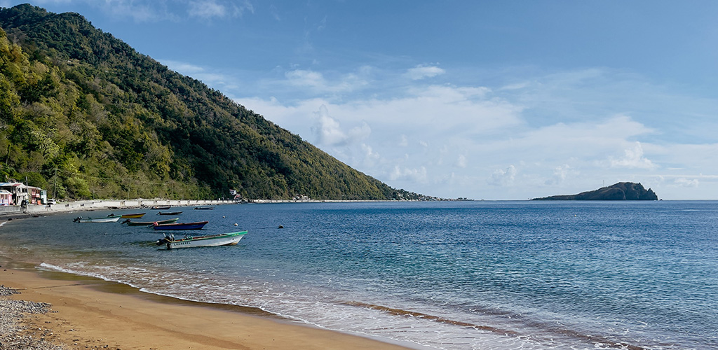 Soufrière Bay village tucked under volcanic slopes above quiet Caribbean water, a south-west postcard of the dominica nature island.