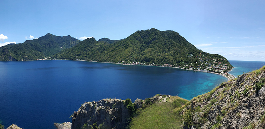 Hiker pausing on a high ridge with Soufrière Bay and Scotts Head below, best hikes in dominica curated day routes from easy waterfalls to hard volcano treks.