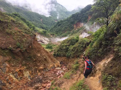 Rugged boiling lake hike trail cutting across open volcanic slopes with distant peaks, boiling lake hike views toward the interior, Dominica.