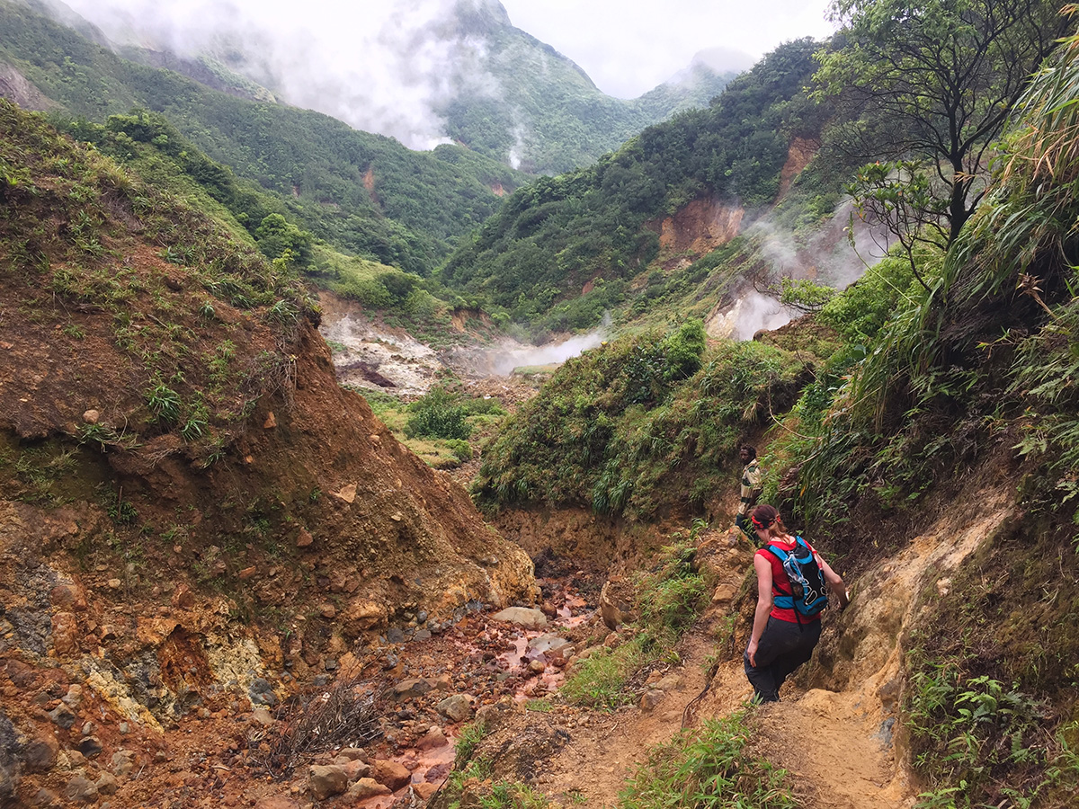 Rugged boiling lake hike trail cutting across open volcanic slopes with distant peaks, boiling lake hike views toward the interior, Dominica.