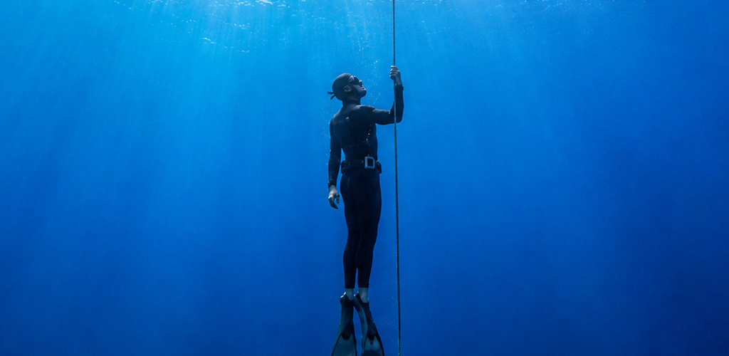 Freediver finning down a clear blue wall above deep water off Dominica, freediving dominica sessions that showcase the island’s dramatic underwater topography.