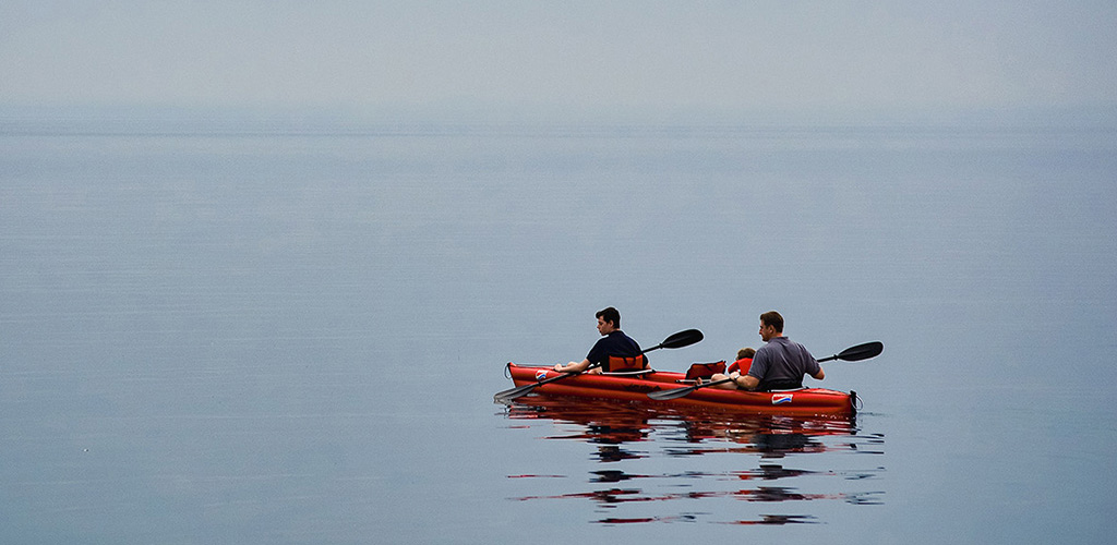 Paddleboarder on glassy Caribbean water at sunset near shore, kayaking in dominica and calm SUP sessions along mangrove creeks and sheltered bays.