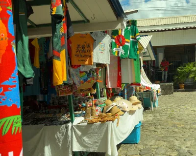 Pedestrians near the tourist information area with historic stone architecture, bay front access for cruise-day visitors in Roseau, Dominica.