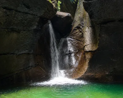 Small waterfall tumbling into the gorge’s shaded pool, titou gorge swimming finish where cold mountain water meets swimmers, Dominica.